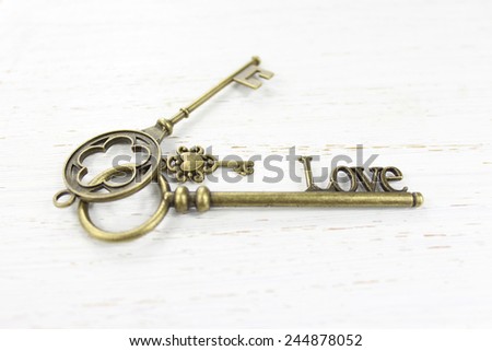 Three brass keys on a white distressed wood background. One key is fashioned with the word Love.