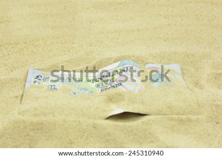 UK Five Pound note covered in sand. Copy space.