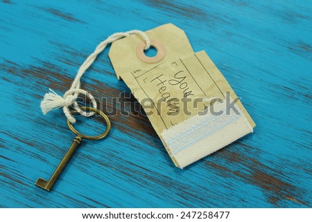 Key with a tag and the handwritten words \'your health\' on it. Rustic blue wooden background.