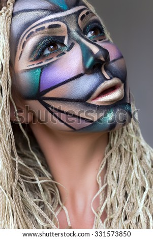 The creative, bright, graphic makeup.  Art makeup. Different colors wild look with braids. Young beautiful model with face art.