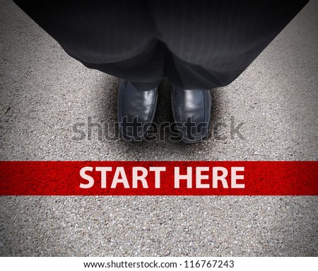 A business man is looking down at his feet with a red race line that says start here to represent a journey,