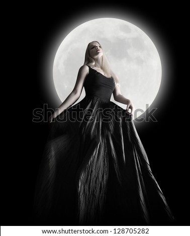A woman is wearing a long black dress moving in the dark night against a full moon for a fashion or mystery concept.