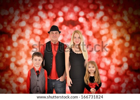 A young family is posing for a Christmas photography portrait against red sparkly lights.