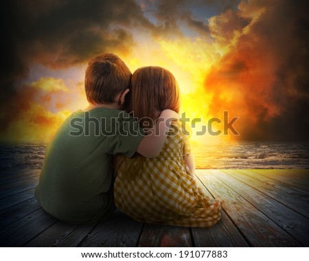 A little boy and girl are hugging and watching the sunset in the sky. The children are sitting on wood for a family, love or vacation concept.