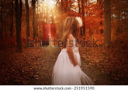 A little child is in the woods wearing a white dress and looking at a glowing red door behind her on a wood path for a mystery or imagination concept.