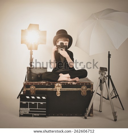 A retro child is holding a vintage camera and focusing with various photography lighting equipment for a director or film concept.
