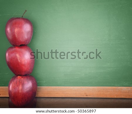 Three red apples are stacked up and leaning against a green school chalkboard. Use the photo for a classroom, school or education concept.