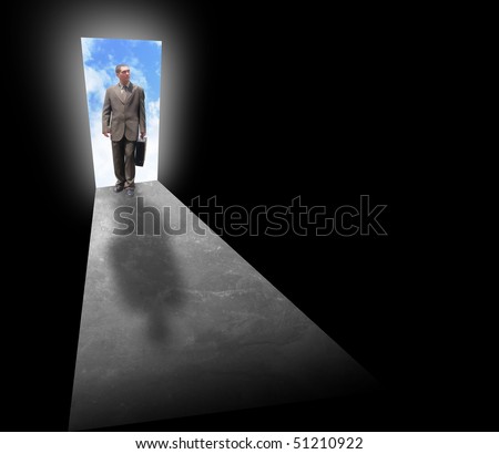 A business man is holding a briefcase and standing at an open door with light behind him. The room is dark and black. Can represent opportunity, fear, risk or success.