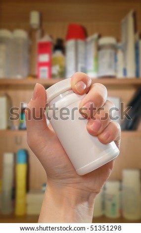 A hand is holding a blank white medical prescription bottle and there is a medicine cabinet in the background with shadow. Photo can be used for addiction, pain or healthcare.