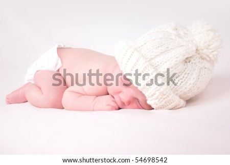 A newborn baby is wearing a white hat and laying down sleeping on a soft white background. Use the photo to represent life, parenting or childhood.