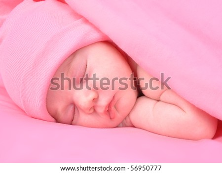 A newborn baby girl is sleeping on a pink background with a blanket. She is wearing a hat. Use it for a childhood, parenting  or innocence theme.
