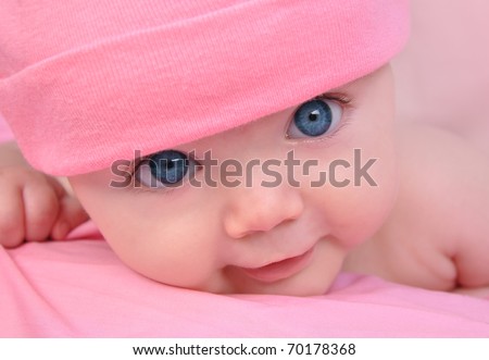 A cute little baby girl is staring up and is on a pink blanket. She is wearing a pink hat and has big blue eyes. Use it for a child, parenting or love concept.