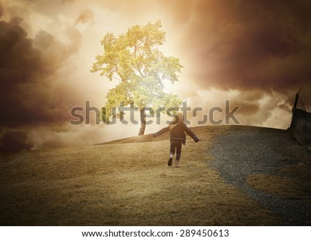 A little child is running up a hill to a glowing tree of light with dark clouds in the background. Use it for a hope, freedom or happiness concept.