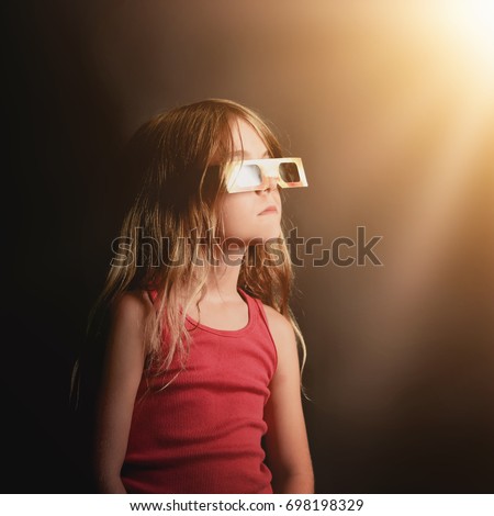 A little girl is looking at the 2017 solar eclipse with protective eye glasses on an isolated background with shadows for a space science concept.