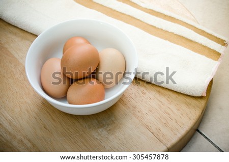 the five eggs in white ceramic bowl and brown strip white towel on wood table