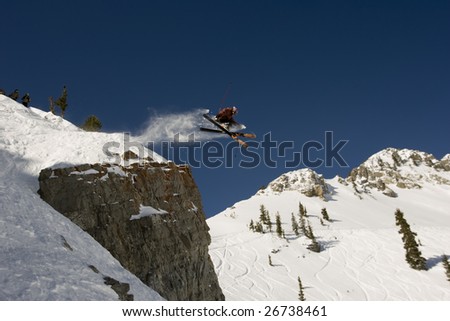 A skier jumping cross tips off cliff with mountain in background