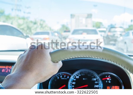 Hand of driver holding steering wheel, with traffic view in the city