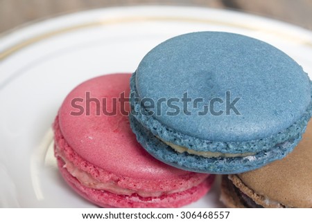 Three colorful macaron - Blue macaron vanilla flavor, pink macaron strawberry flavor and brown macaron chocolate flavor on the plate, focusing on blue macaron on top.