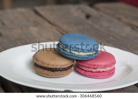 Three colorful macaron - Blue macaron vanilla flavor, pink macaron strawberry flavor and brown macaron chocolate flavor on the plate, blue macaron on top.