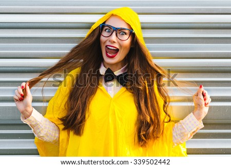 Colorful emotional summer outdoor funny beautiful pretty girl in yellow raincoat with fun sunglasses long hair red lips black bow-tie and comic smile laughing posing and having fun show tongue out