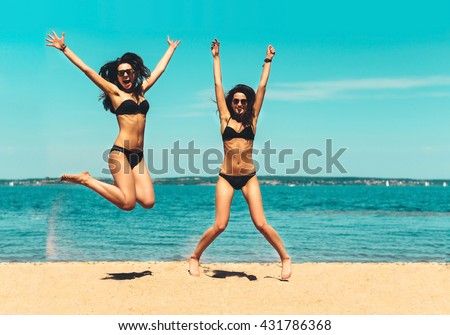 Two Attractive Girls in Bikinis Jumping on the Beach. Best Friends Having Fun, Summer vacation holiday Lifestyle. Happy women jumping freedom on white sand.