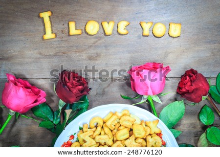 Happy Valentine\'s Day red roses on dark recycled wood background with word I Love You dessert