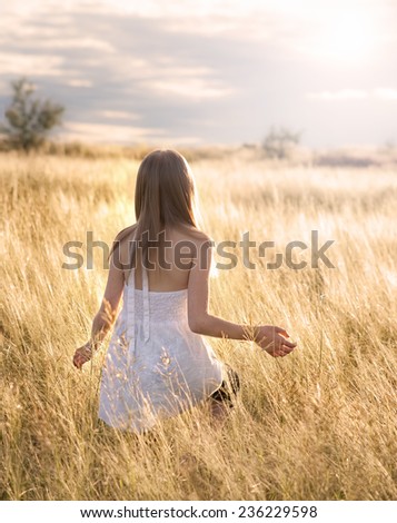 Girl walking in a field of gold colored grass at sunset.  Girl is walking away from the camera.  Softly lit scene.  Title and caption are \