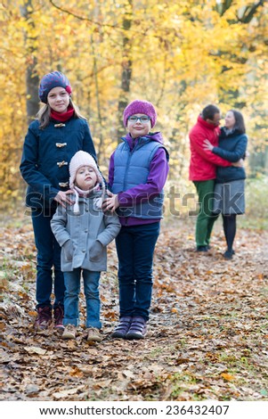 Beautiful scene of young happy family in autumn forest, five members: three sisters looking at camera and blurred parents behind