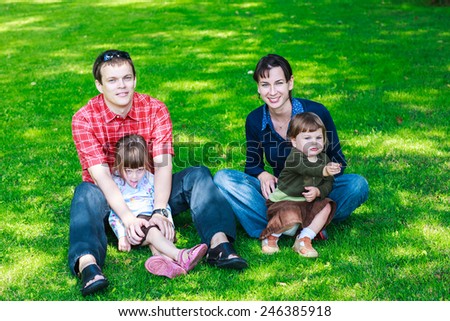 Happy family on the grass. happy family of four sitting on grass during summer rest - parents and two cute little daughters