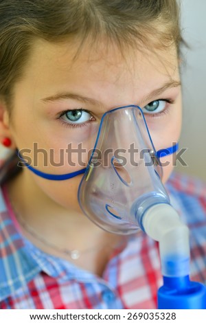 Girl with asthma inhaler. Girl with asthma (or allergy) problems making inhalation with mask on her face. Inhalation treatment of respiratory diseases. Shallow depth of field