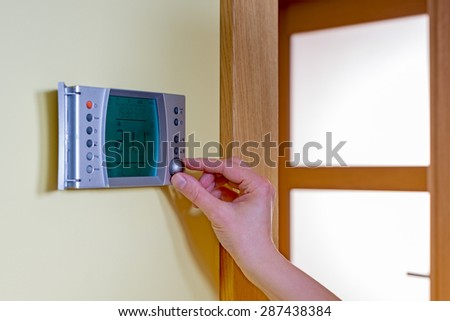 Closeup of a woman\'s hand setting the room temperature on a modern programmable thermostat - with copy space. Save energy and money concept