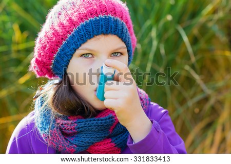 Girl Using Inhaler on a autumn day - to Treat Asthma Attack. Inhalation treatment of respiratory diseases. Shallow depth of field. Allergy concept. Asthma child.
