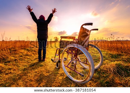 Miracle recovery: young girl gets up from wheelchair and raises hands up. Overjoyed young girl  standing up from a wheelchair outdoors. Shot in meadow. Recovery concept