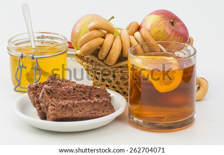 Glass cup of tea with lemon, basket of apples, bagels, honey and chocolate cake