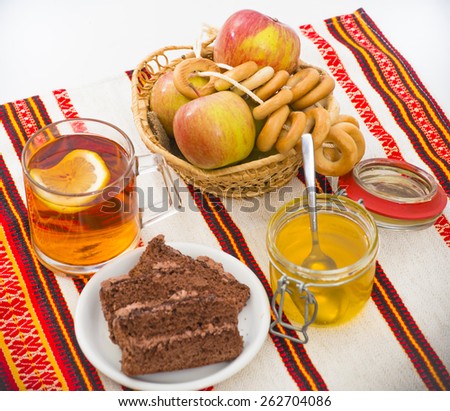 Glass cup of tea with lemon, basket of apples, bagels, honey and chocolate cake