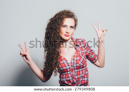 Confident girl showing peace in front of white wall. Girl wearing a plaid shirt and leather pants/Confident girl showing peace