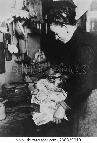 This Berlin woman, realizing that fuel costs money, is starting the morning fire with marks...\', Germany, ca 1920s.