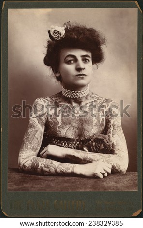 Portrait of a woman showing images tattooed on her body, the Plaza Gallery, Los Angeles, California, 1907.