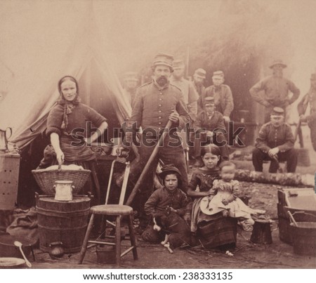 The Civil War, woman with sleeves rolled up holding basket, with a soldier and three children, soldiers in the background, camp of 31st Penn Infantry near Washington DC, photograph, February, 1862.