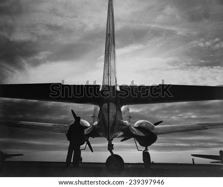 World War II, soldier beside WWII airplane at sunrise, circa early 1940s.