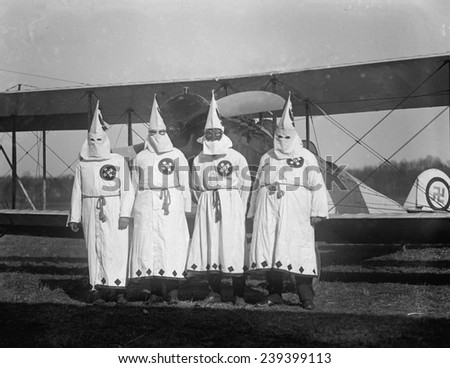 Four hooded Ku Klux Klan members pose in from of their airplane which bears a swastika emblem. 1922 photo.