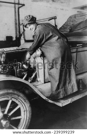 Female auto saleswoman, Rosalie Jones, attends to auto mechanics in a duster and hat in 1925.