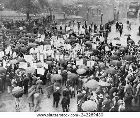 The Great Depression. A crowd of depositors protest in the rain at the Bank of United States after its failure. Signs demand bank stockholders be taxed to repay small depositors. New York City 1931.