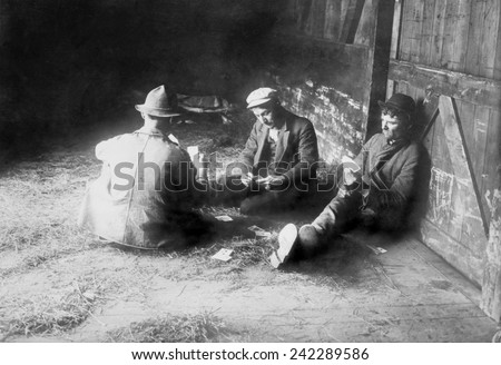 Tramps traveling in a freight car pass the time playing cards. Migrant laborers hopped box cars to seek work. Ca. 1910.