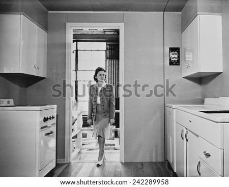 Women enters a modern 1940s kitchen with white enameled metal cabinets. The housing was built by the government for workers on TVA and other Defense projects in World War II. Dec 1941.