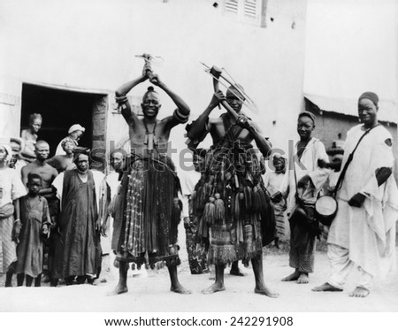 Two itinerant medicine men on a street in the village of Abeokuta, Southern Nigeria. Performing a \'hoe dance\' a traditional Hausa agricultural dance. Ca. 1935.