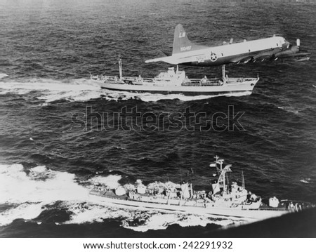 Soviet freighter ANESOV, escorted by a United States Navy plane and the destroyer, USS BARRY, as it leaves Cuba loaded with missiles signaling the end of Cuban Missile Crisis. October 1962.