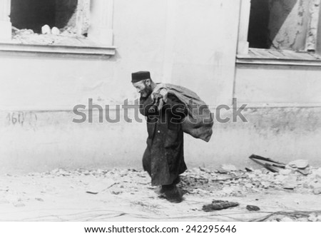 A solitary Jewish man carrying a sack walking past bomb damaged buildings in Poland in the early days of World War II. 1939-40.