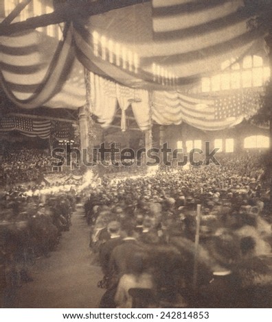 Interior view of a large convention hall filled with seated people. The 35-star flags decorating the hall allow the image to be dated as 1865.