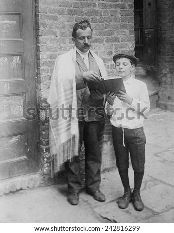 Jewish man wearing a prayer shawl and boy reading from Hebrew Bible on Yom Kippur, in New York City. Ca.1910.